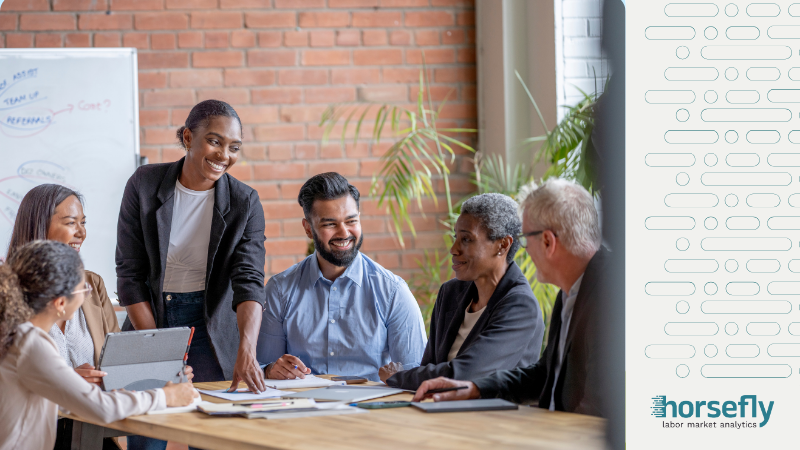 Image shows a group of people having a discussion around a desk for the blog entitled - The Evolution of Workforce Analytics: Transformative Workforce Technology