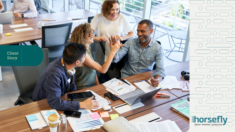 Image shows four work colleagues celebrating and high-fiving at their desks